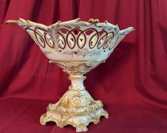Ornate porcelain compote featuring an openwork reticulated rim, gold gilt accents, floral motifs, and a pedestal base. The dimensions are approximately 13 inches tall by 17.5 inches long. Finely decorated with delicate detailing.
