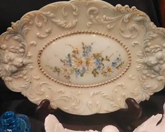 White milk glass pitcher with grape and leaf motif, an ornate oval platter with floral center, a pair of white bird figurines, a small blue glass bell, and a FireKing milk glass bowl marked "MADE IN USA FIREKING WARE OVEN PROOF."