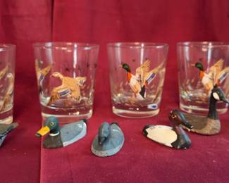 Glass tumblers decorated with flying mallard ducks and miniature hand-carved duck decoy figurines. Also included is a small wooden bucket featuring a painted duck motif.