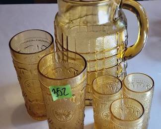 Amber glass beverage set including one pitcher with a check pattern and tumblers with a floral motif. The pitcher measures approximately 8.5 inches high. Three smaller tumblers are approximately 4 inches high.