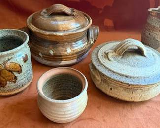 Studio pottery pieces: covered casseroles with handles, two small bowls, a floral-motif cylindrical vessel, and two handled pitchers. Some pieces are artist signed on the base. Various earth-tone glazes throughout the group. 