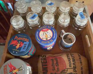 Woodstock Creamery Co. wood crate marked property of Mick-or-Mack, containing three Planters and nut-themed tins, a burlap bag labeled Planters Roasted Peanuts, an aluminum trophy cup, and eight glass canning jars with lids. Signs of wear visible on crate and containers.