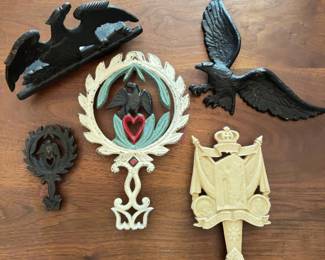  cast iron wall plaques and ornaments, each depicting eagles, heart motifs, or commemorative designs. Includes a Jamestown 350th anniversary plaque, painted heart and eagle plaques, and two black eagle plaques, each with mounting points on the back.