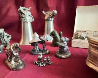 metal animal head figural stirrup cups, a set of six embossed silver napkin rings with floral and lion motifs, a silver-plated trinket box with royal crest and red fabric lining, and a group of small animal figurines in metal.