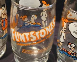 Glass tumblers featuring Flintstones characters and branded as Flintstones Children's Chewable Vitamins. Each glass displays cartoon illustrations, character quotes, and measures approximately 4 inches tall.