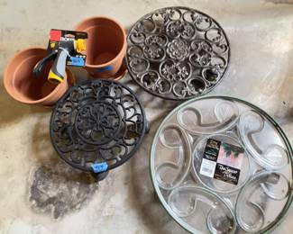 Metal rolling plant caddies with decorative patterns, a glass plant caddy with swirl compartments, terracotta clay flower pots, and a packaged adjustable hose nozzle.