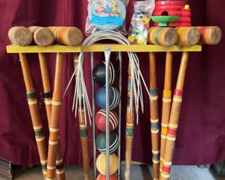 Sears croquet set including eight mallets with wood handles, colored bands, six striped croquet balls, metal wickets, and yellow wood stand. Also included are a plastic M&M's gumball machine and two sealed Disney toys. Items show wear from use.