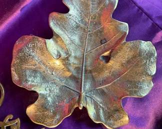Brass items including a leaf-shaped decorative tray with a marked underside, ornate brass trivets with monogram designs, and a brass candlestick. 