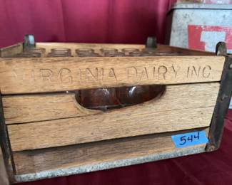Clear glass milk bottles featuring Virginia Dairy logos in a wooden carrier marked "VIRGINIA DAIRY INC." and a metal Virginia Dairy box. Includes multiple bottle sizes. Wear and residue present on bottles and crates from previous use.
