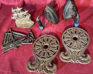 Cast iron sailboat figures, a cast iron ship doorstop or decorative piece, two cast iron trivets with scroll designs, and two small cast iron irons with handles. Items show surface wear and rust areas.