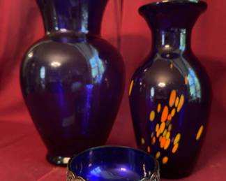 Cobalt blue glass vessels, including two vases and a small bowl. The taller vase measures approximately 11.5 inches. One vase features yellow and orange decorative dots, and the small bowl includes a pierced silver overlay rim. All pieces display vibrant cobalt blue coloring