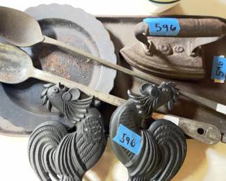 Cast iron platter, a small cast iron iron, metal serving spoons, a set of rooster-shaped black cast iron decor pieces, and ceramic bowls decorated with rooster and foliage motifs. Items show surface wear and oxidation on metal surfaces.