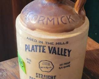 Stoneware jug marked McCormick Platte Valley, labeled as aged in the hills and containing straight corn whiskey. Features original brown glazed handle and printed distillery info. Holds 4/5 quart, 100 proof.