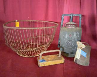 large wire basket, a metal hand lantern with glass globe, a rectangular yellow metal weight or block with handle, and a cowbell with cloth strap. 