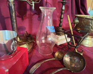 A brass pedestal bowl with engraved designs and handles, a green glass and metal lamp, glass hurricane lamp chimneys, metal ladles, a metal urn, a metal cup, and a metal and glass table lamp with hurricane shade.