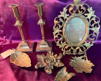 Ornate brass picture frame with easel back, square-base brass candlesticks, and brass leaf and flower-shaped decorative dishes.