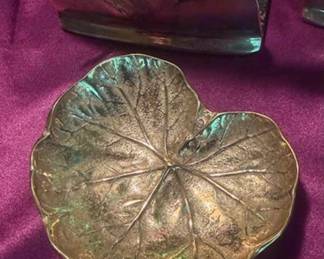 Decorative brass items including a pair of turned candlesticks, Royal Coat of Arms wall plaque, horse head bookends, and a leaf-form dish. All pieces are crafted from brass with detailed designs. 
