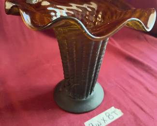 Amber glass vase featuring a flared, ruffled rim and textured vertical ribbing on the body. The base is circular with a matte finish. Approximate dimensions are 9 inches wide and 8 inches tall. 