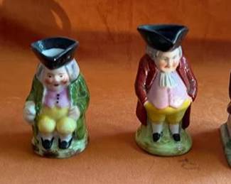 Hand-painted ceramic Toby jugs, each modeled as a seated man in period dress with tricorn hats, most with handles at the back. Marked "Germany" on one base. Each features colorful glazed details.