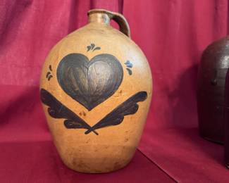 Four assorted handled jugs including a 9-inch tan jug with heart and feather motif, a brown 8.5-inch jug, a large 10-inch speckled brown jug, and an I.W. Harper Kentucky Whiskey ceramic advertising jug. 