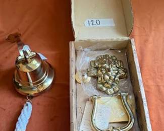 Brass lion head door knocker in its original packaging from India Metal Crafts along with a brass bell marked "Made in India for Authentic Models Handmade." The bell includes a braided pull cord.