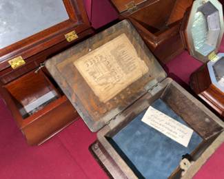 Wooden jewelry or keepsake boxes in various shapes and finishes, each with hinged lids and brass handles or hardware. Interiors are lined, and one box features an old paper diagram affixed inside the lid.