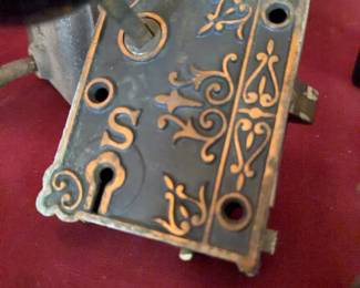 Iron sad irons with fixed handles and two decorative cast iron mortise door locks with black round knobs. One lock features ornate scrollwork. Items show oxidation, wear, and paint loss consistent with use.