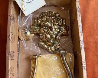 Brass lion head door knocker in its original packaging from India Metal Crafts along with a brass bell marked "Made in India for Authentic Models Handmade." The bell includes a braided pull cord.