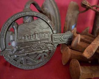 A cast iron railroad-themed plaque, two metal flat irons, a wooden-handled Richmond Joe Company ice tool, a bundle of rusted railroad spikes, and a metal letter stamp set. Items show surface wear and rust.