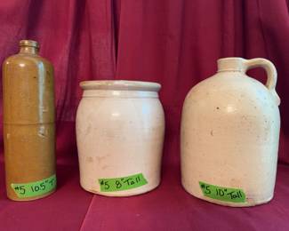 Three stoneware pottery vessels, including a brown bottle measuring 10.5 inches tall, a beige crock 8 inches tall, and a cream-colored jug with handle and spout 10 inches tall.