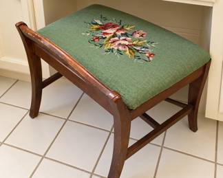 Charming vintage wooden vanity or dressing stool featuring a green needlepoint-style upholstered seat with a colorful floral design. The dark wood frame has gently curved legs and supportive crossbars, with light age-related wear that adds character. A lovely accent piece for a bedroom, dressing table, or entryway!