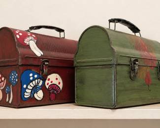 Vintage metal lunch boxes with domed tops, carrying handles, and latch closures. One features colorful, hand-painted mushrooms, while the other has a rustic green finish with decorative accents. Both show natural age and wear, adding wonderful retro character—perfect for collectors, storage, or unique home décor!