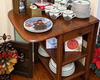 Charming holiday entertaining collection featuring Christmas tree-pattern dinnerware with coordinating mugs, plates, bowls, and serving pieces. Also includes decorative holiday plates, boxed ornaments, glass vases, a festive display stand, and a versatile wooden rolling kitchen cart with drawer and open shelving. Perfect for seasonal gatherings, decorating, or collectors!