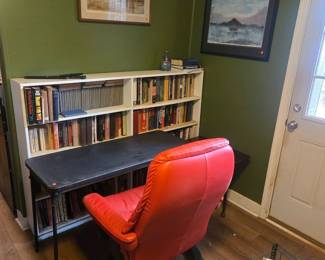 Folding table, red chair and numerous books and artwork.