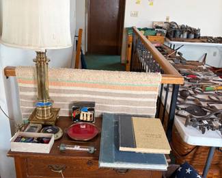 Antique wood commode, brass table lamp, vintage atlases, woven rug, butter churn base, vintage tools