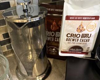 Crio Bru brewed cacao setup featuring a 34 oz stainless steel French press, bags of ground cacao