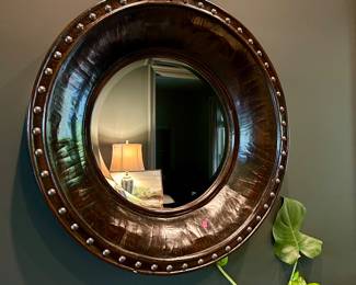 Round wall mirror with a deep, dark wood frame and nailhead trim