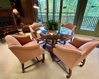 Round glass-top dining table with woven cane detail and carved wood pedestal base, including four upholstered caster chairs
