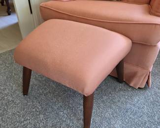 Coral upholstered ottoman with wood legs, tufted chair behind