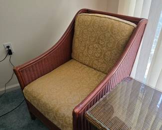 Wicker armchair with gold damask cushions, next to wicker table