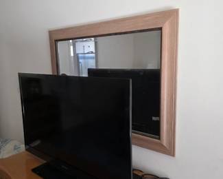 Flat-screen TV and large wall mirror with light wood frame