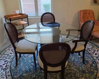 Round glass dining table with 4 caned-back chairs, area rug