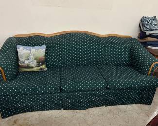 The image shows a traditional green patterned fabric sofa with a wooden accent trim along the top backrest and armrests. • Style: Traditional / vintage 3-cushion sofa • Pattern: Dark green fabric with a small repeating light-colored motif (dots or diamonds) • Details: Exposed wood curved top rail and arm accents, skirted base