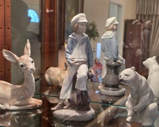 Lladro porcelain sailor boy holding a model sailboat, displayed with deer and polar bear figurines.