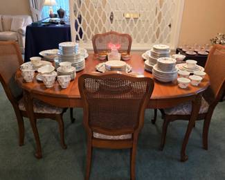 Traditional wood dining table and cane-back chairs with vintage china, cups, saucers and serving pieces