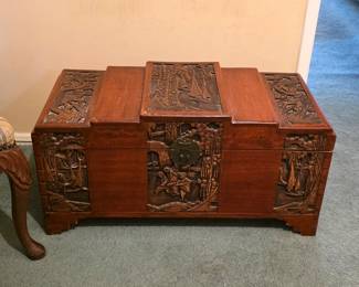Carved Asian-style wooden trunk with decorative panels, figural scenes and raised feet.