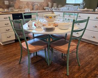Hexagonal kitchen table and green metal chairs with upholstered seats, displayed with china and glassware.
