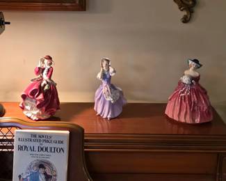 Royal Doulton porcelain figurines displayed atop the piano, featuring seated and standing ladies in colorful gowns.