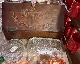 Assortment of vintage kitchen and serving pieces including a vintage wooden bread box, pink Depression-style glass, clear pressed glass serving dishes, colorful ceramic canisters, and assorted pitchers and kitchenware.