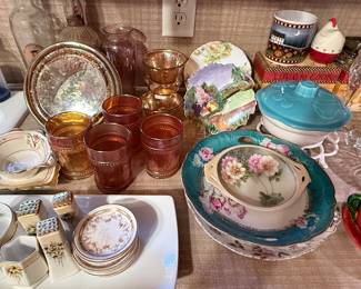 Assortment of vintage tableware including amber glass tumblers and goblets, floral china serving pieces, teacups and saucers, salt and pepper shakers, pressed-glass serving dishes, covered casserole dish, and decorative ceramics. A colorful mix of vintage kitchen and entertaining pieces.
